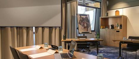 Una sala de conferències amb una pantalla gran, taules de fusta, cadires, un portàtil i un projector.