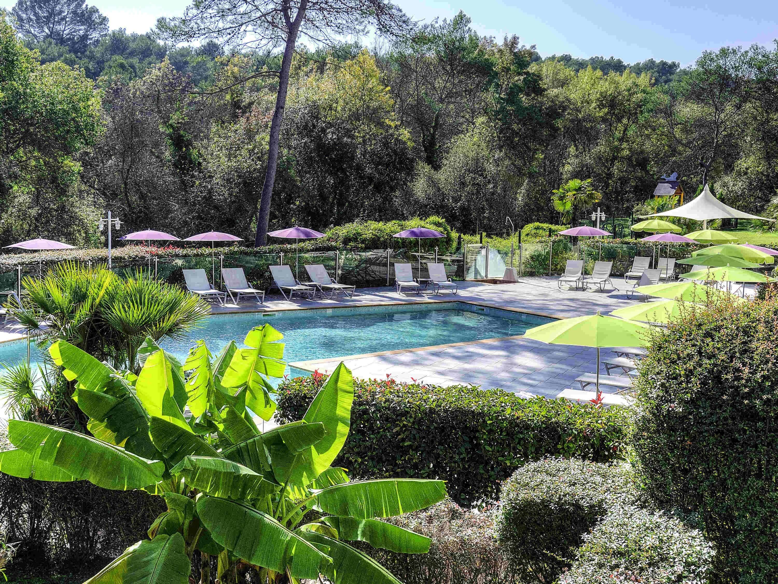 Area piscina con lettini e ombrelloni, circondata da vegetazione lussureggiante.