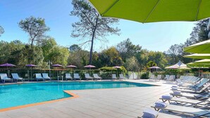 Un espace aménagé au bord de la piscine, avec des chaises longues et des parasols, entouré d’arbres.