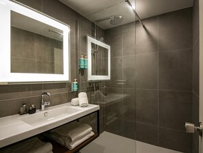 Une salle de bain moderne avec un grand miroir, un lavabo, une douche et un porte-serviettes.