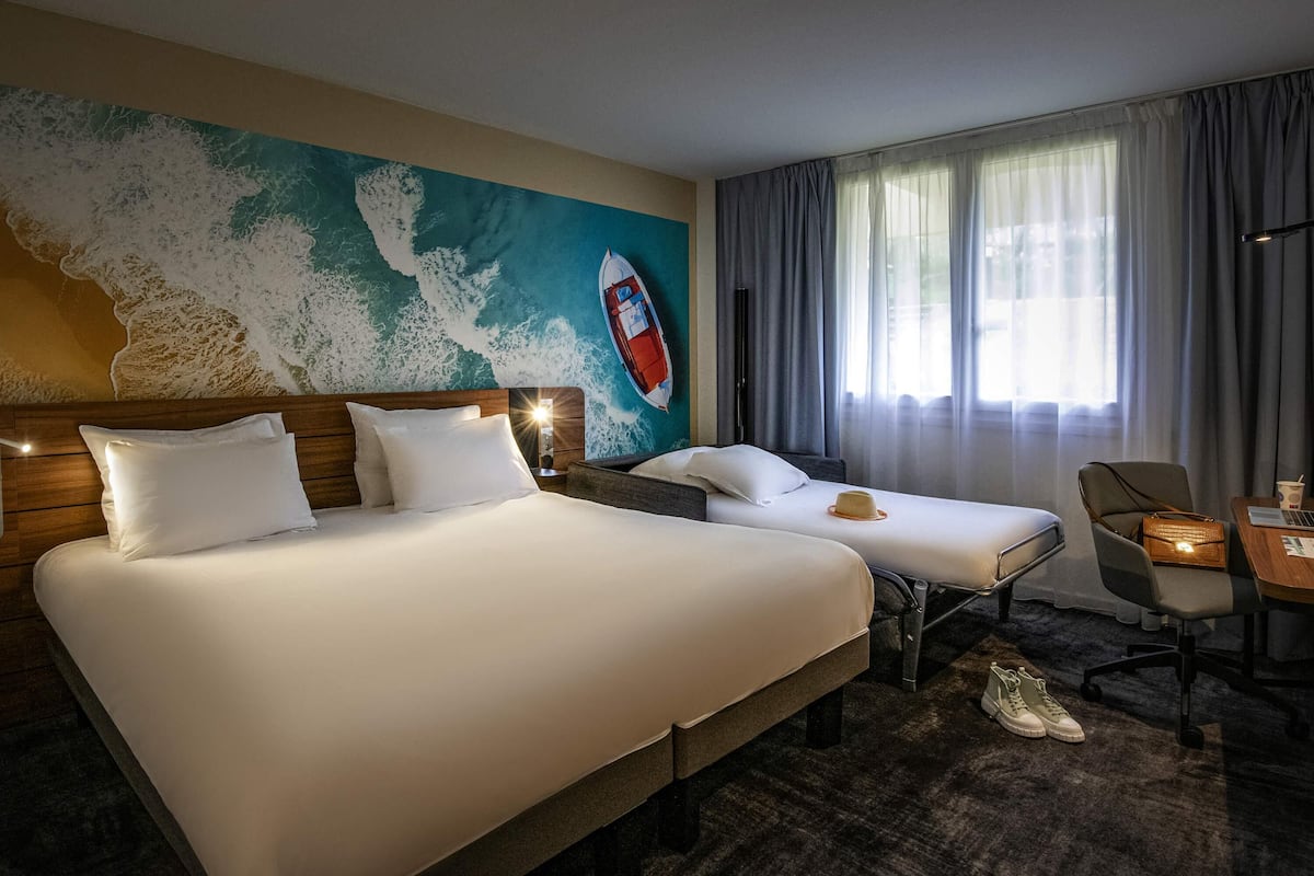 Een hotelkamer met twee bedden, een muurschildering van een boot, een raam met gordijnen en een bureau met een stoel.