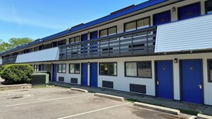 A multi-story motel with blue and white exterior walls, a parking lot, and a small green bush.