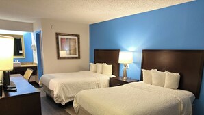 A hotel room with two beds, a desk, a chair, a lamp, a framed picture, and a blue wall.
