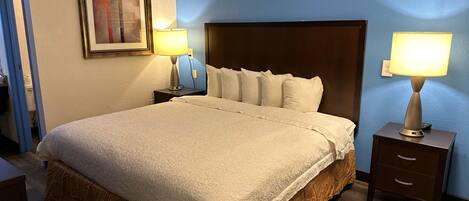 Habitación de hotel con una cama grande, dos mesitas de noche, una lámpara de noche, un cuadro en la pared y una pared de acento azul.