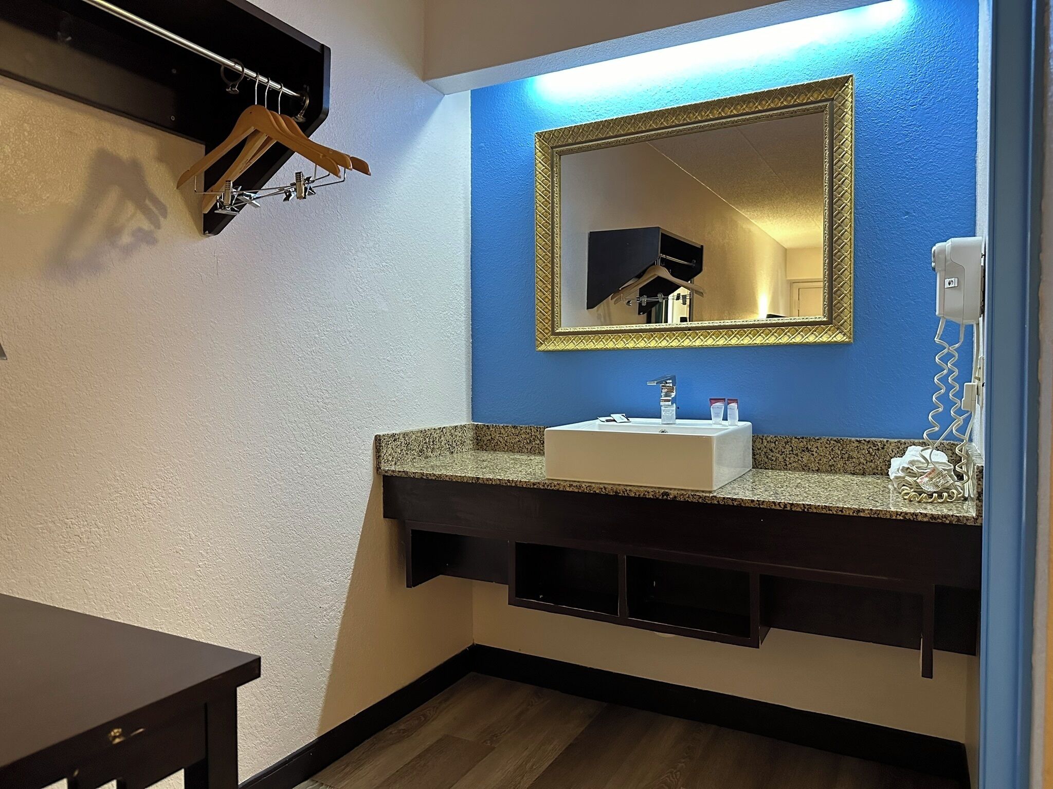 Une salle de bain avec un mur d’accent bleu, un grand miroir, un lavabo et un téléphone.