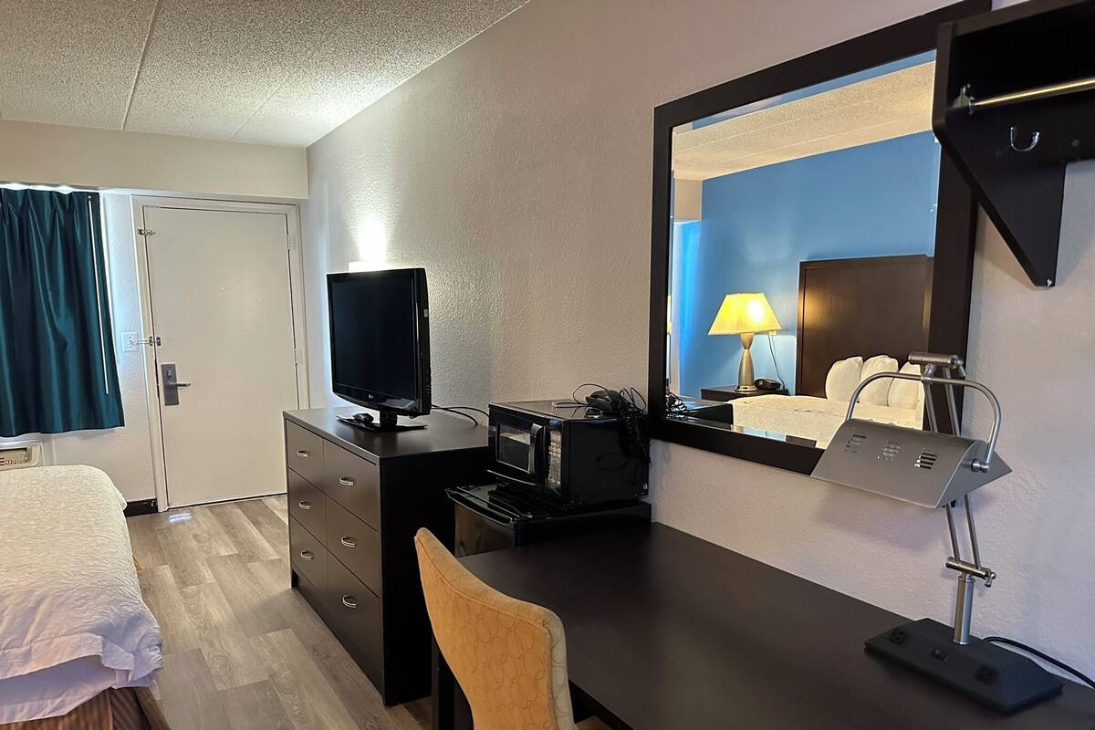 A hotel room with a bed, a desk with a computer, a TV, and a mirror.