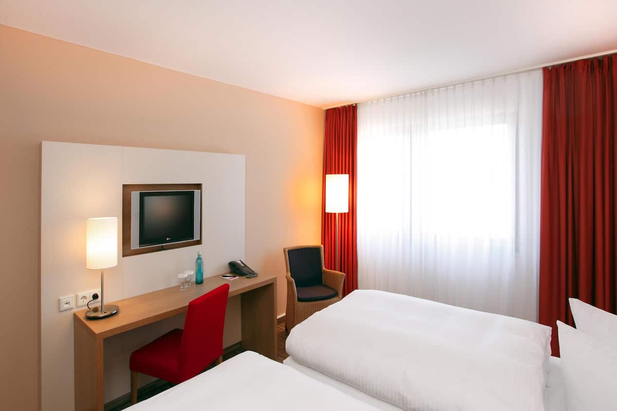A hotel room with a desk, chair, TV, and two beds.