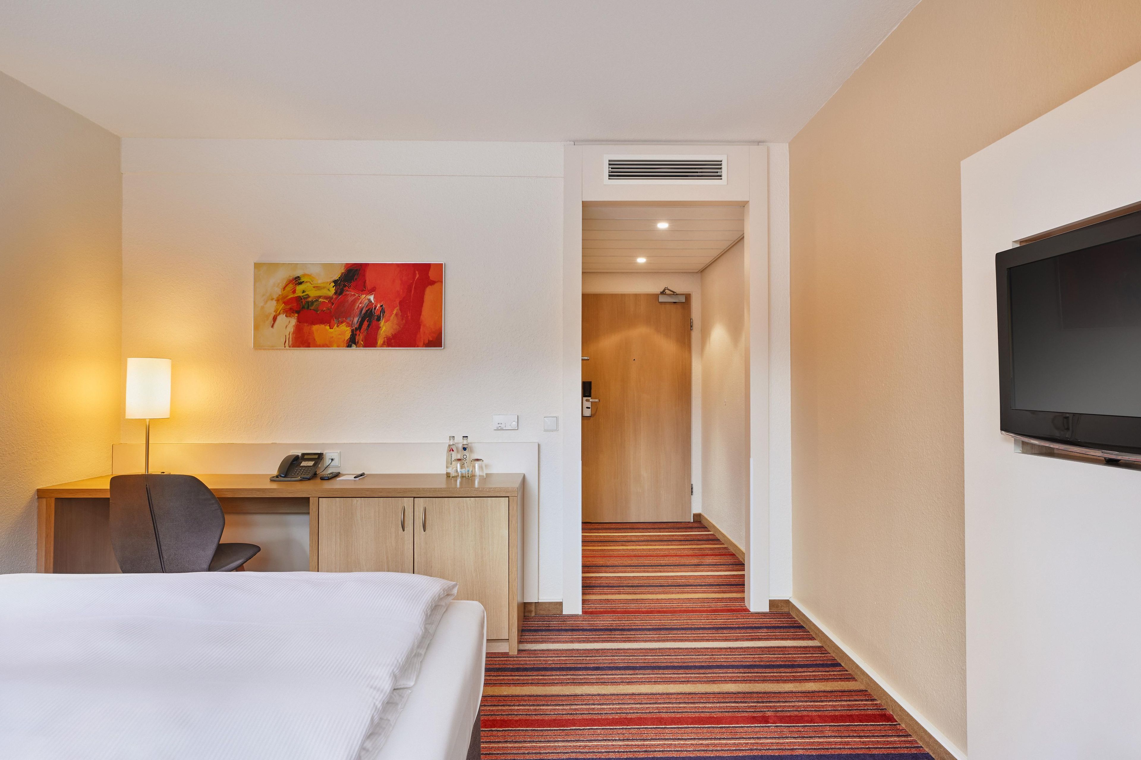 Une chambre d’hôtel avec un lit, un bureau, une chaise, un téléphone et un tableau au mur.