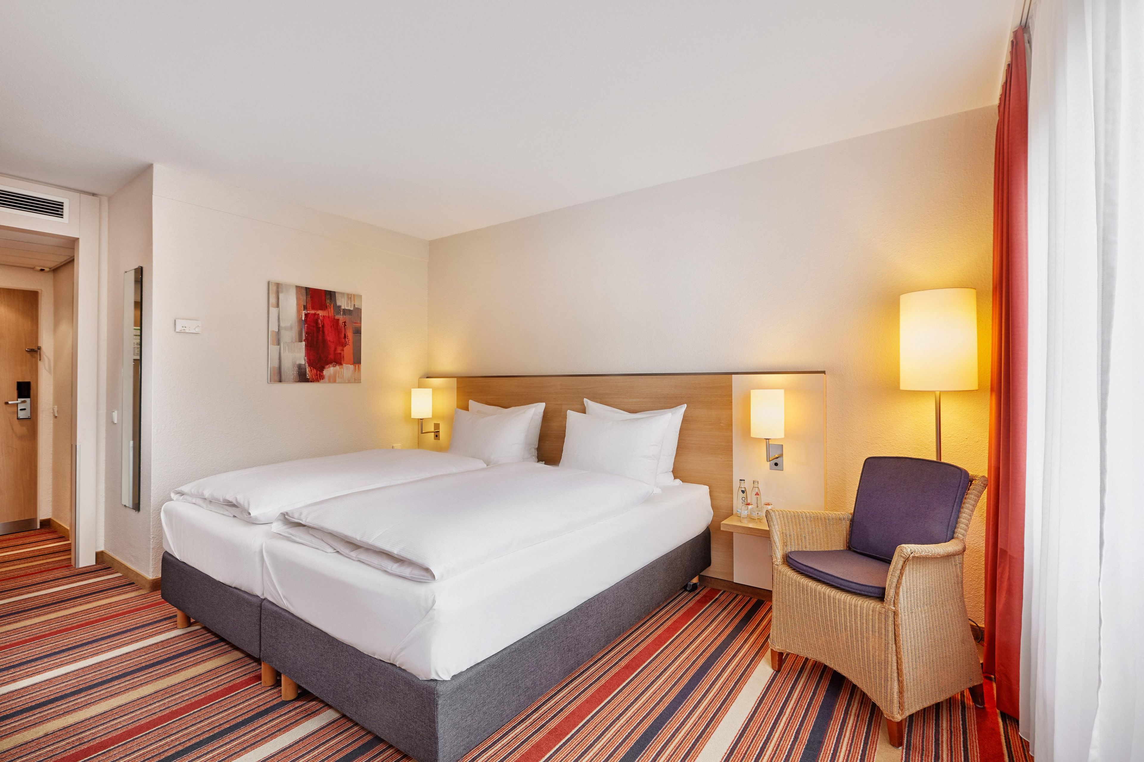 A hotel room with a large bed, two bedside lamps, a chair, and a painting on the wall.