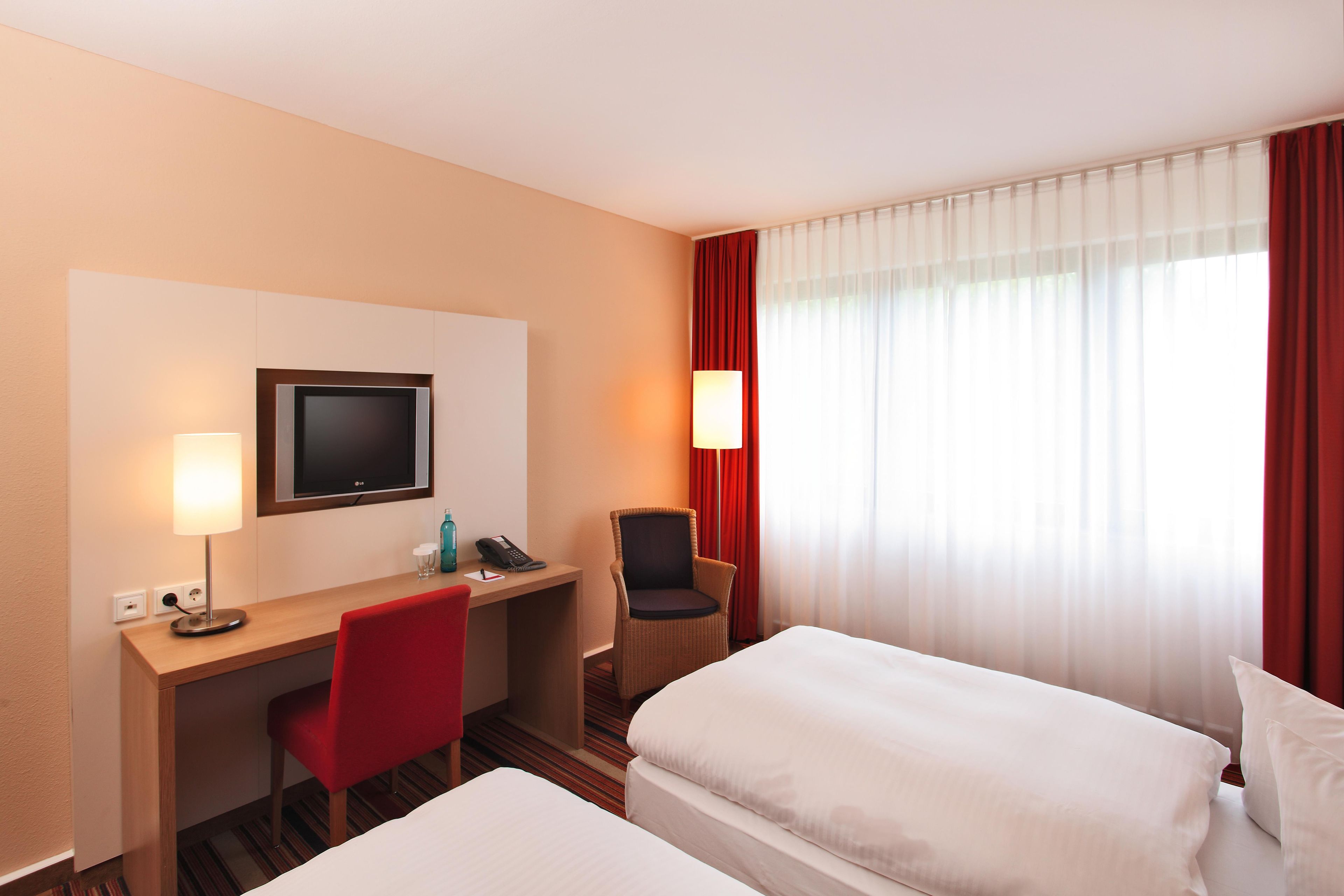 Ein Hotelzimmer mit Schreibtisch, zwei Betten, einem Fernseher und einem fenster mit Vorhängen.
