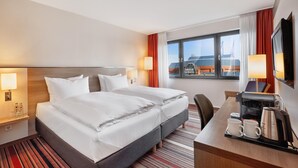 Une chambre d’hôtel avec un lit, des lampes de chevet, un bureau avec une machine à café et une fenêtre avec des rideaux.