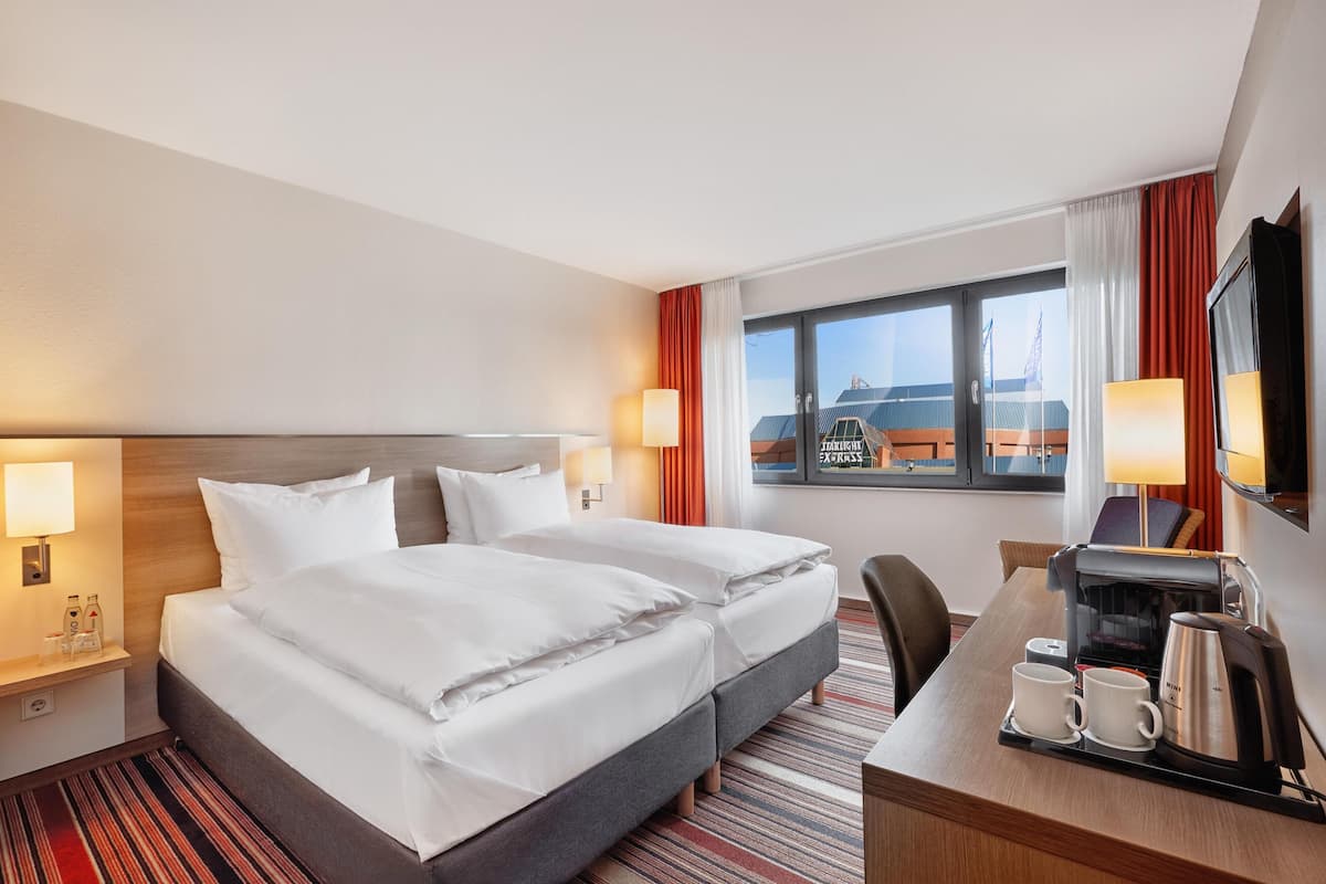 A hotel room with a bed, bedside lamps, a desk with a coffee maker, and a window with curtains.