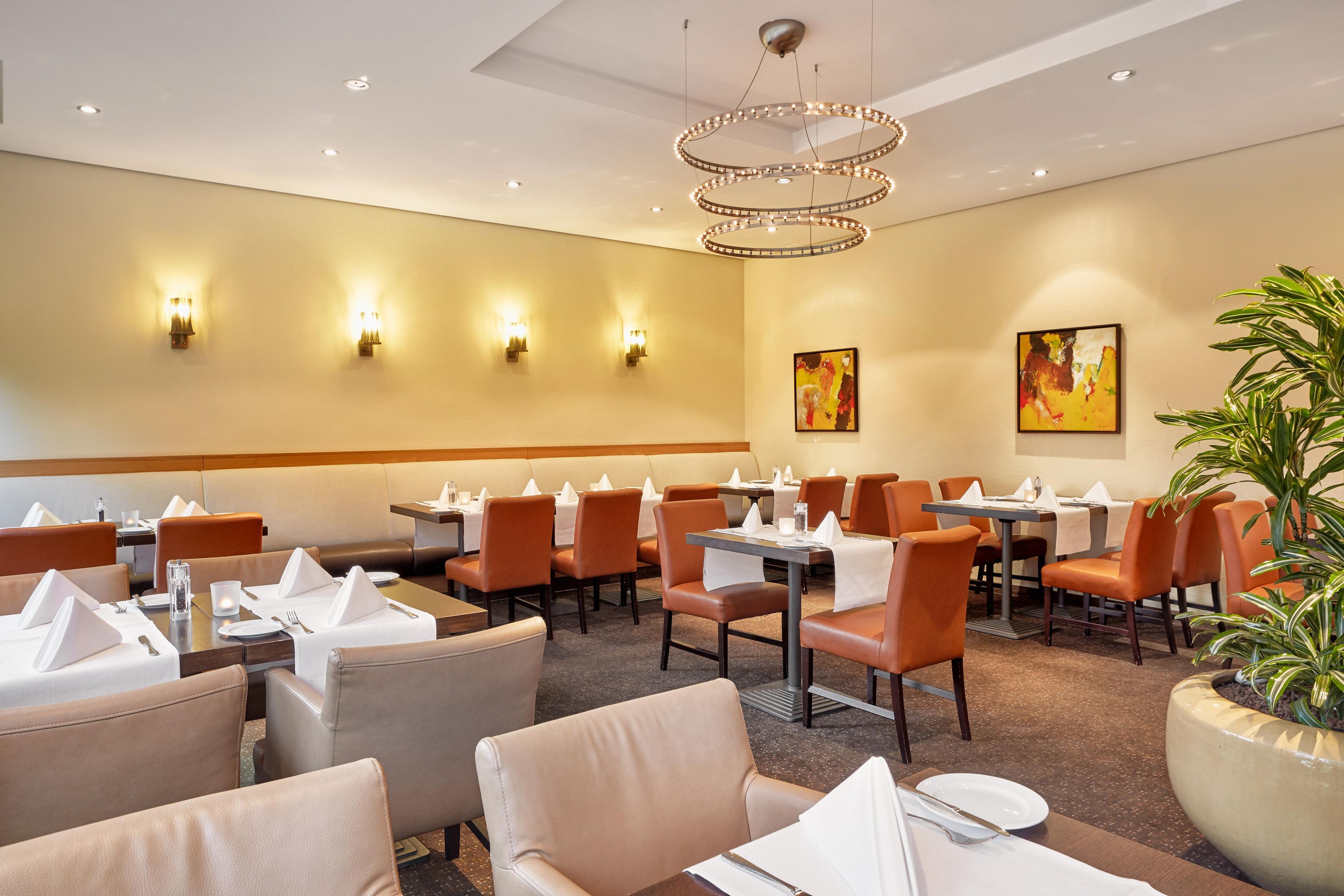 Ein Hotel-Speisesaal mit gedeckten Tischen, Wandleuchten und einer großen Topfpflanze.
