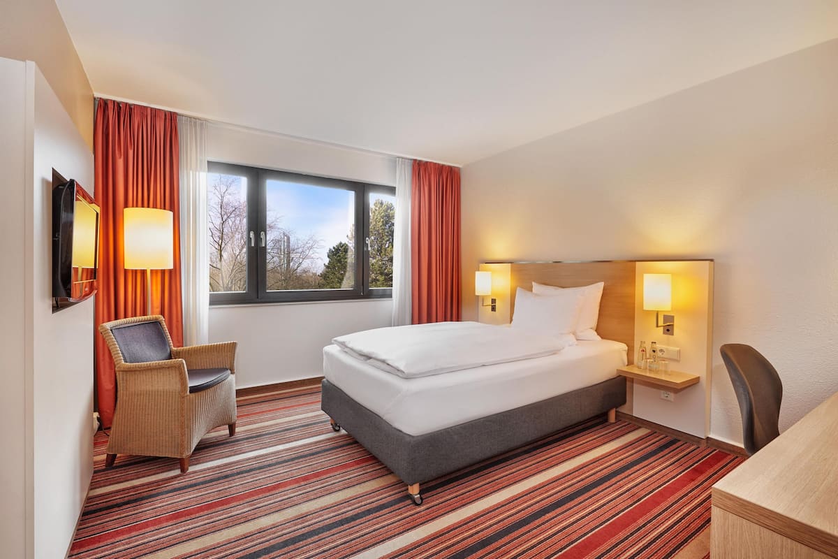 A hotel room with a bed, two bedside lamps, a chair, a desk, and a TV.