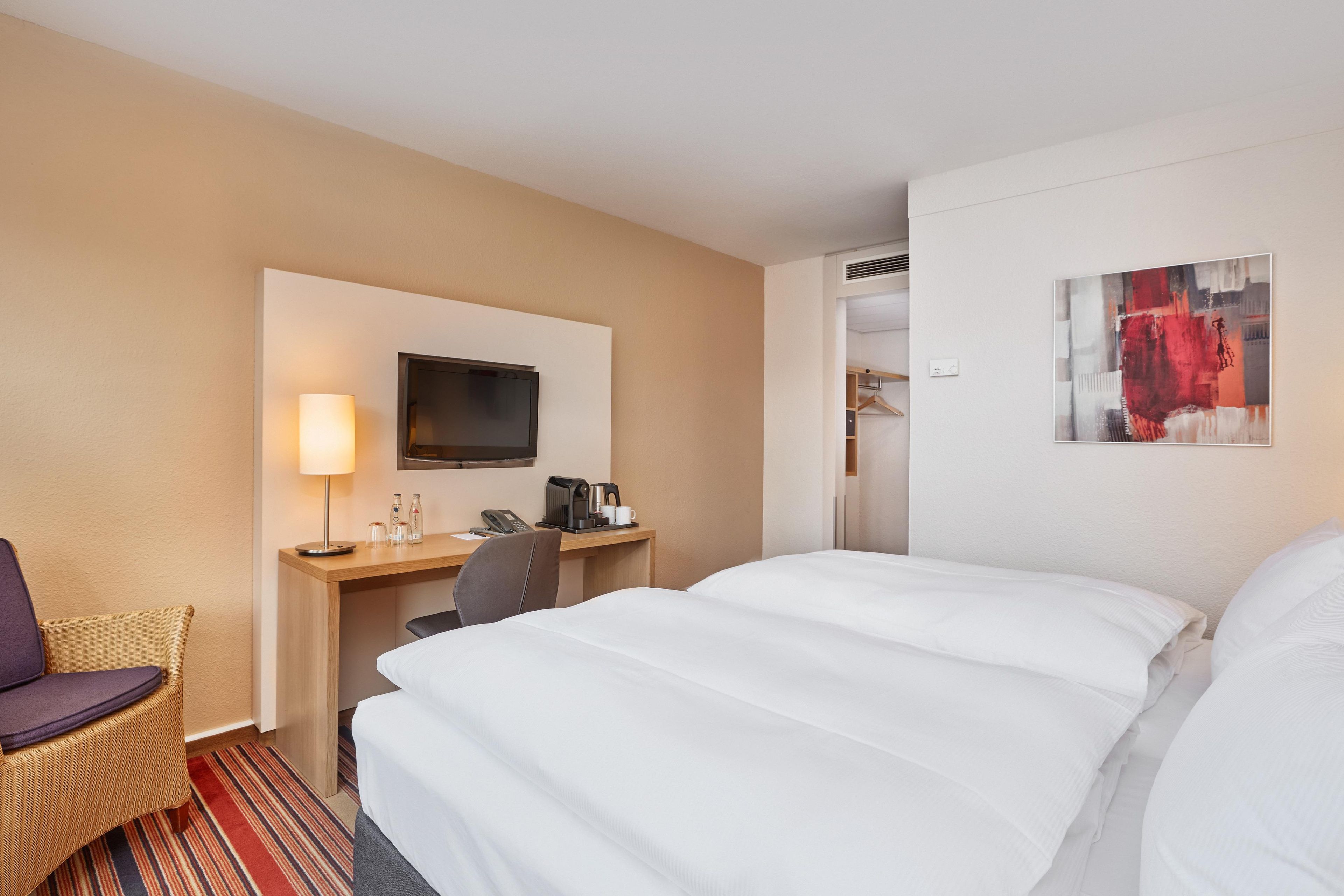 Una habitación de hotel con una cama, un escritorio con una silla, un televisor y un cuadro en la pared.