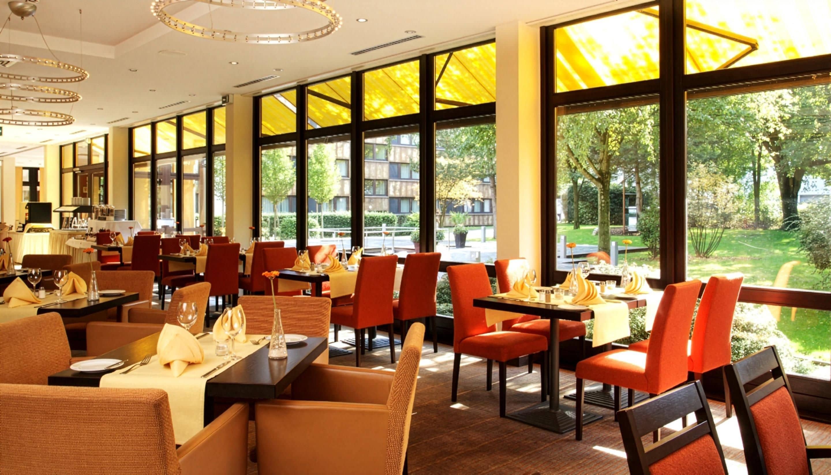 Un restaurante con varias mesas y sillas, ventanas amplias y vistas al exterior.