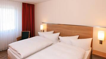 Una habitación de hotel con una cama doble, dos lámparas de noche, una silla y un ventanal con cortinas.