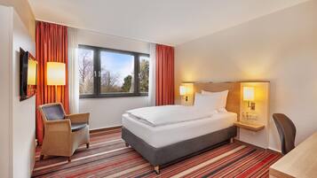 A hotel room with a bed, a chair, a desk, and a window with curtains.