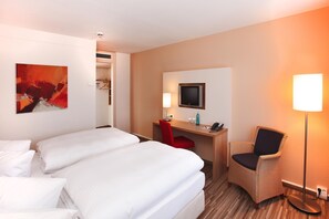 Una habitación de hotel con dos camas, un escritorio con una silla, un televisor y una lámpara.