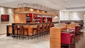 Un espace bar moderne doté d’un long comptoir, de nombreux tabourets et d’un coin salon avec des tables et des chaises.