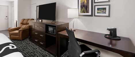 A hotel room with a bed, a desk with a computer, a TV, a chair, a coffee maker, and framed pictures on the wall.