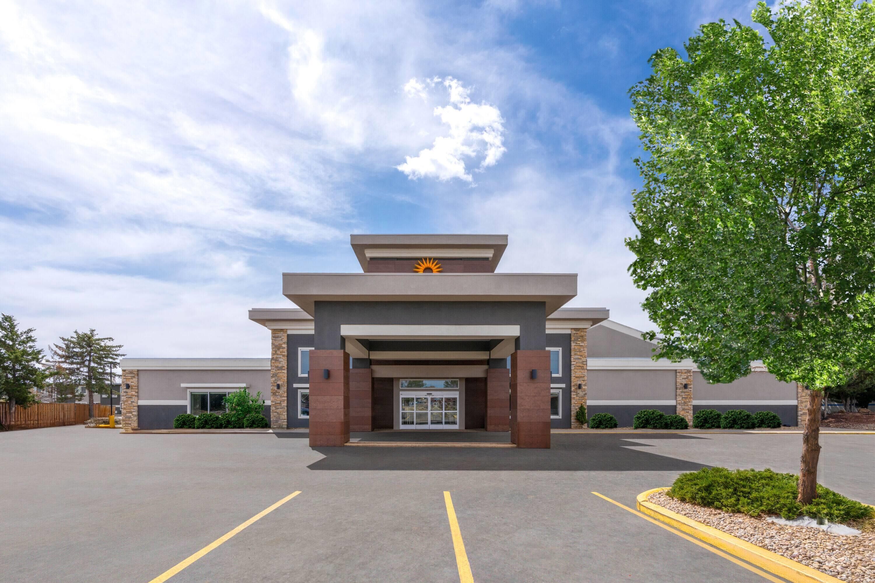 A modern building with a flat roof, a central entrance, and a parking lot in front.