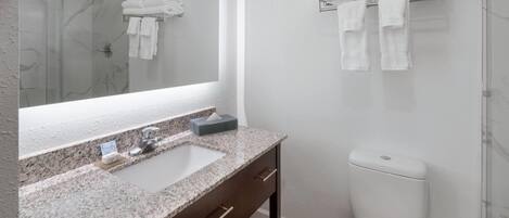A modern bathroom with a granite countertop, a large mirror, a toilet, and a towel rack.