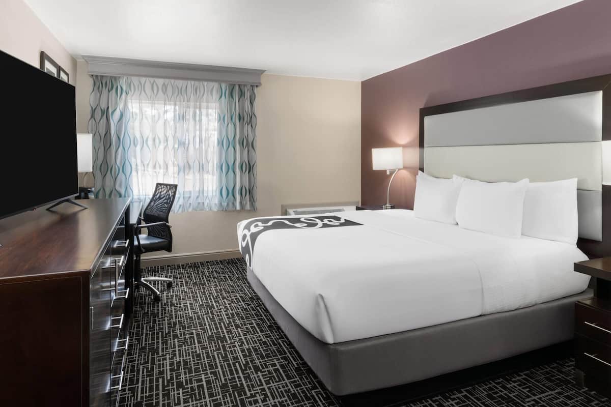 A hotel room with a large bed, a desk with a chair, a TV, and a window with curtains.