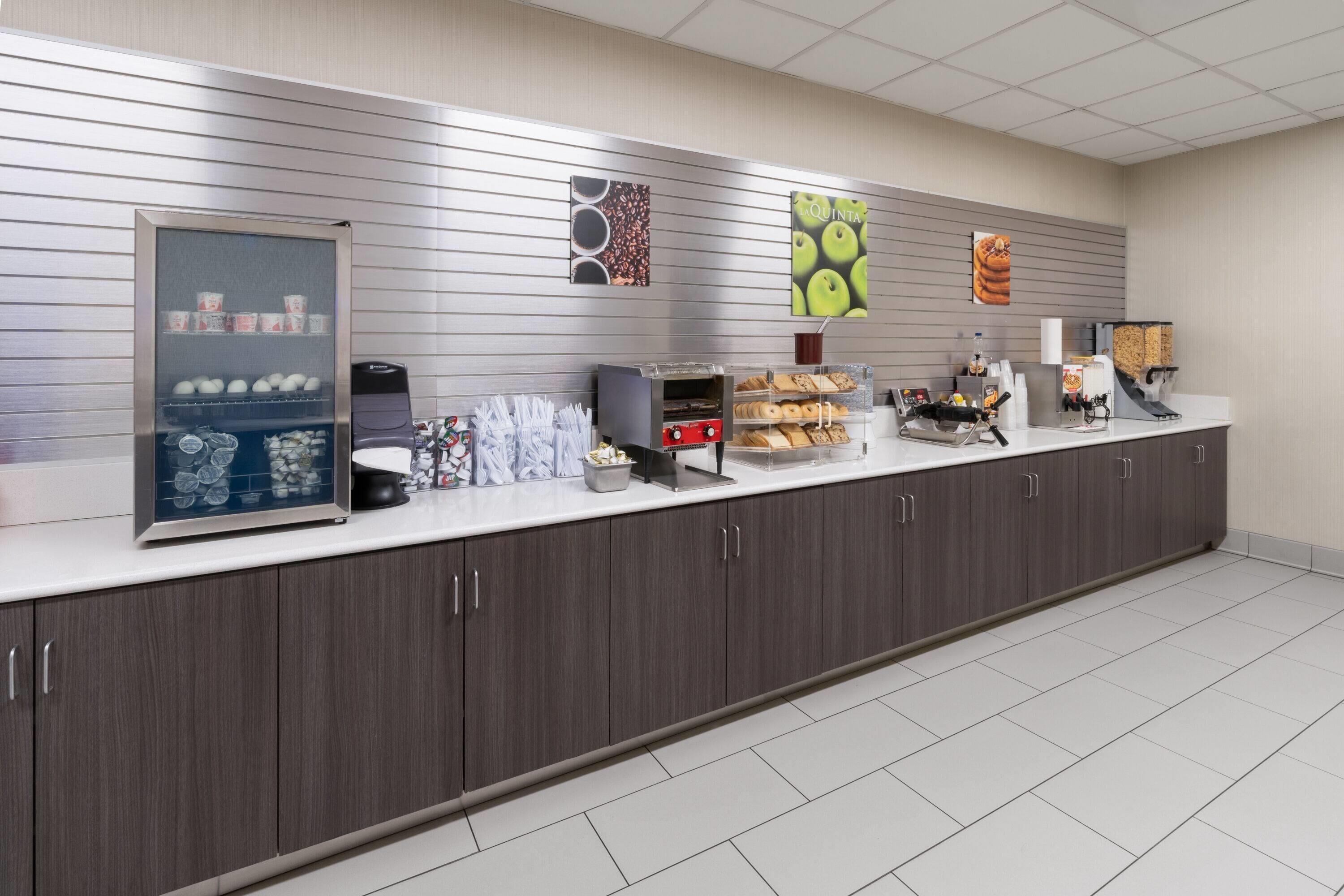 Un espace de petit-déjeuner en libre-service, équipé d'un présentoir réfrigéré, de machines à café et d'une variété d'aliments.