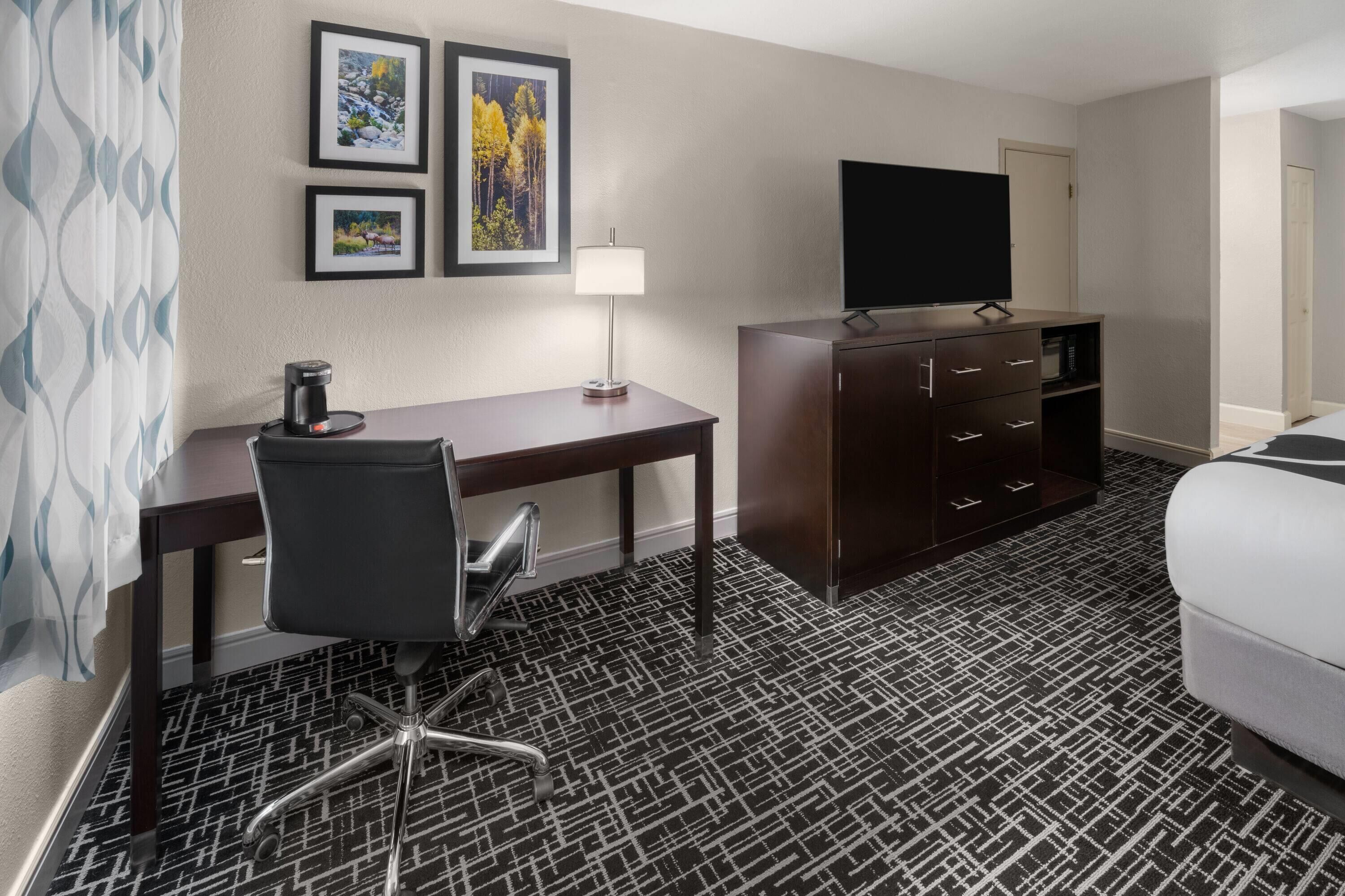 A hotel room with a desk, chair, TV, and a bed.