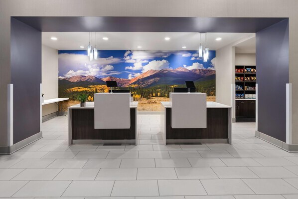 A reception area with a mountain landscape mural, two reception desks, and a bookshelf with various items.