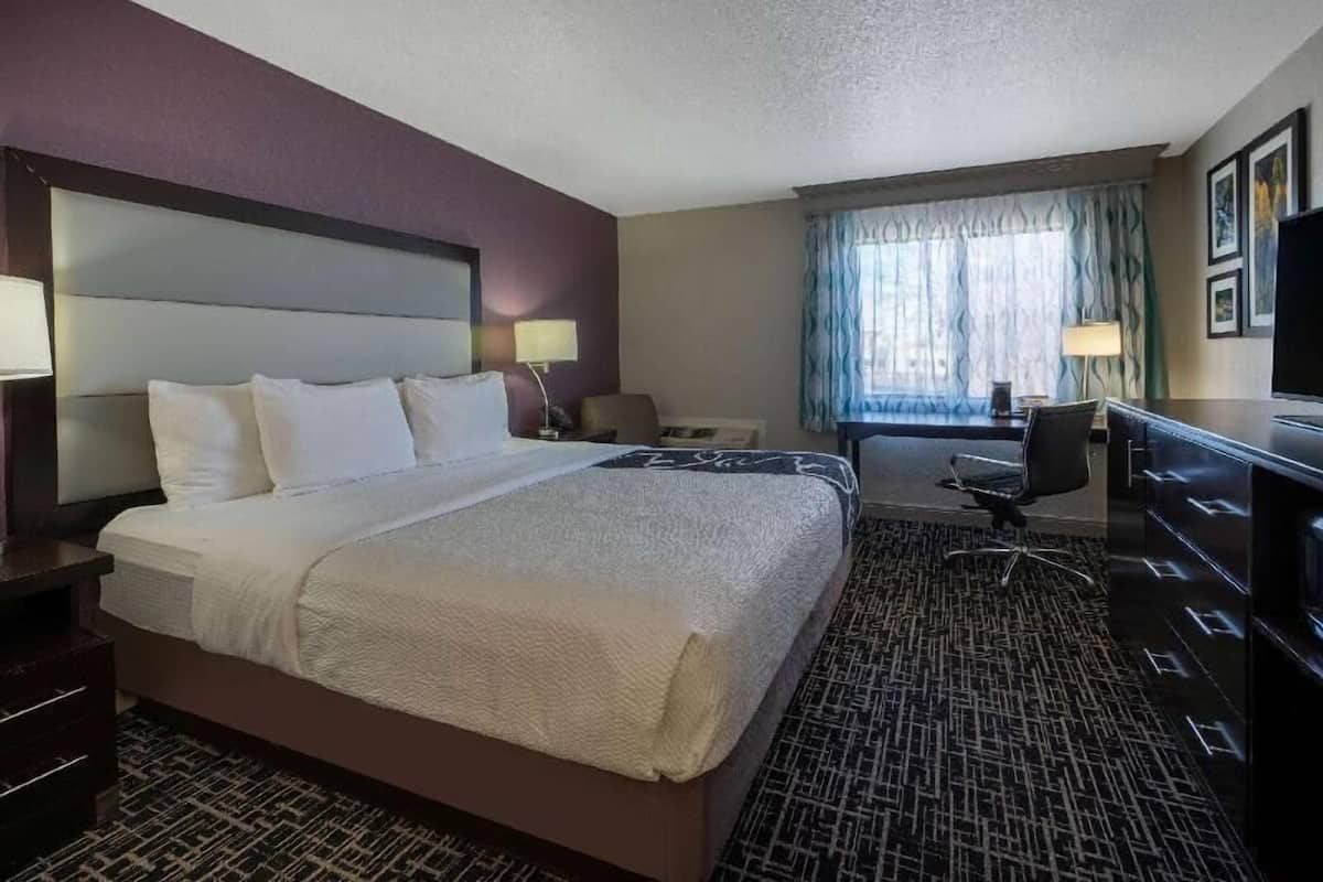 A hotel room with a large bed, a desk, a chair, and a television.