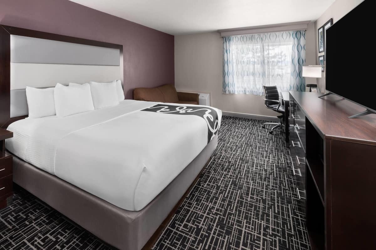 A hotel room with a large bed, a desk, a chair, and a television.