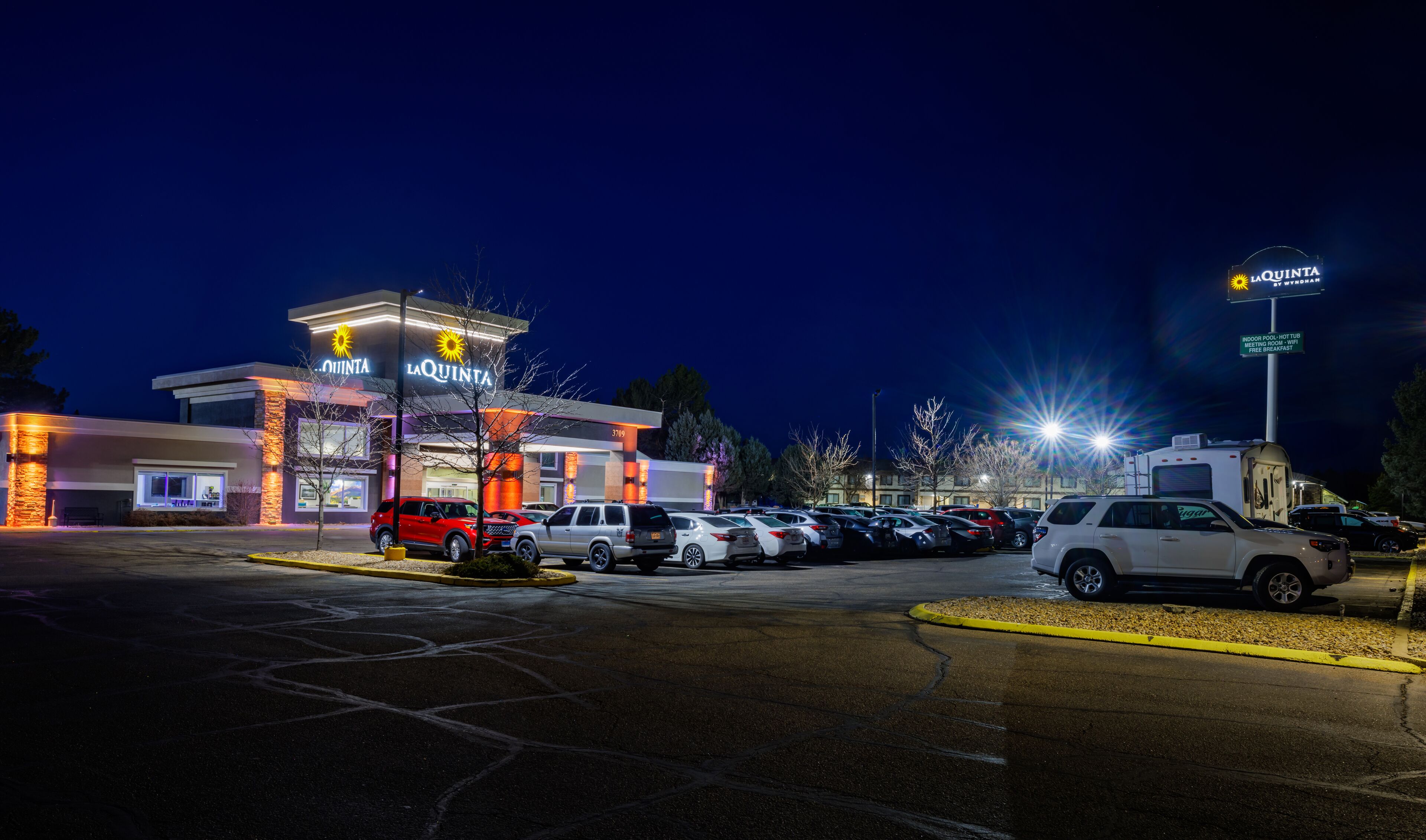 A hotel with a modern design, a parking lot, and a sign indicating amenities like a hot tub and free breakfast.