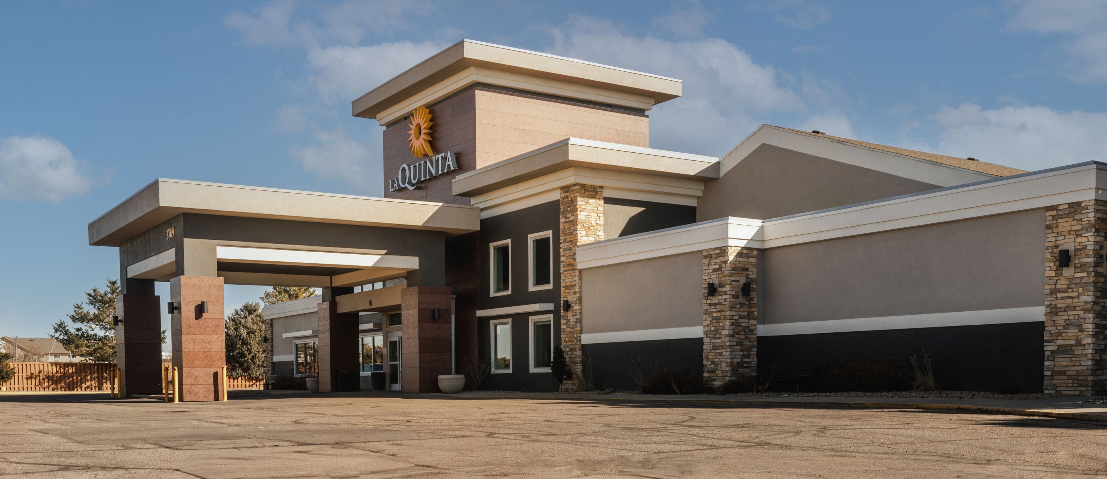A modern hotel entrance with a prominent 'La Quinta' sign, a covered parking area, and a stone facade.