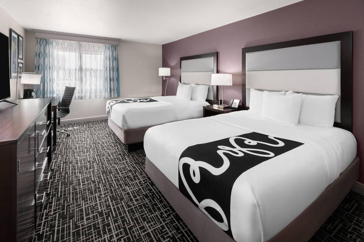 A hotel room with two beds, a desk, and a chair.