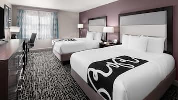 A hotel room with two beds, a desk, and a chair.