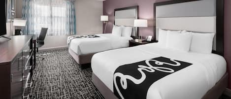 A hotel room with two beds, a desk, and a chair.