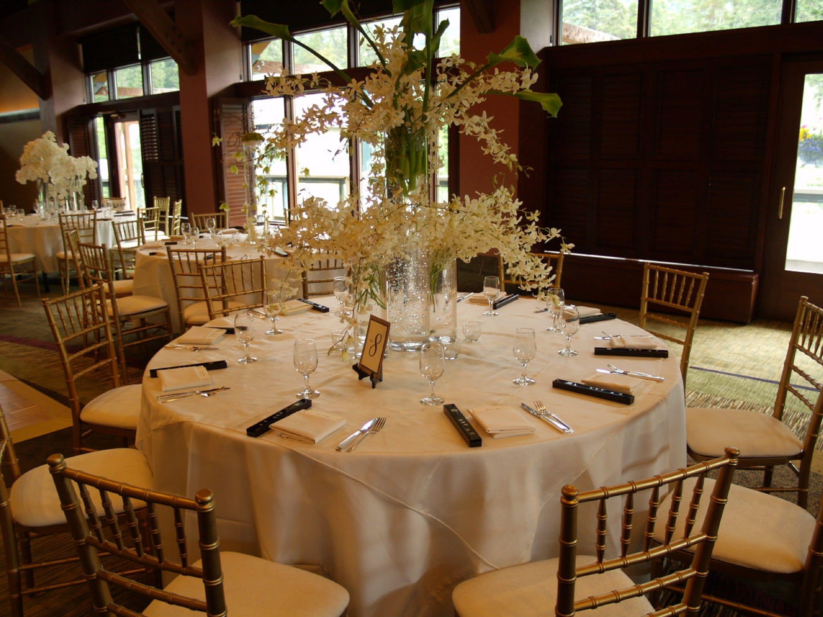 A round table set for a formal event with chairs, a vase of white flowers, and a sign indicating table number 8.
