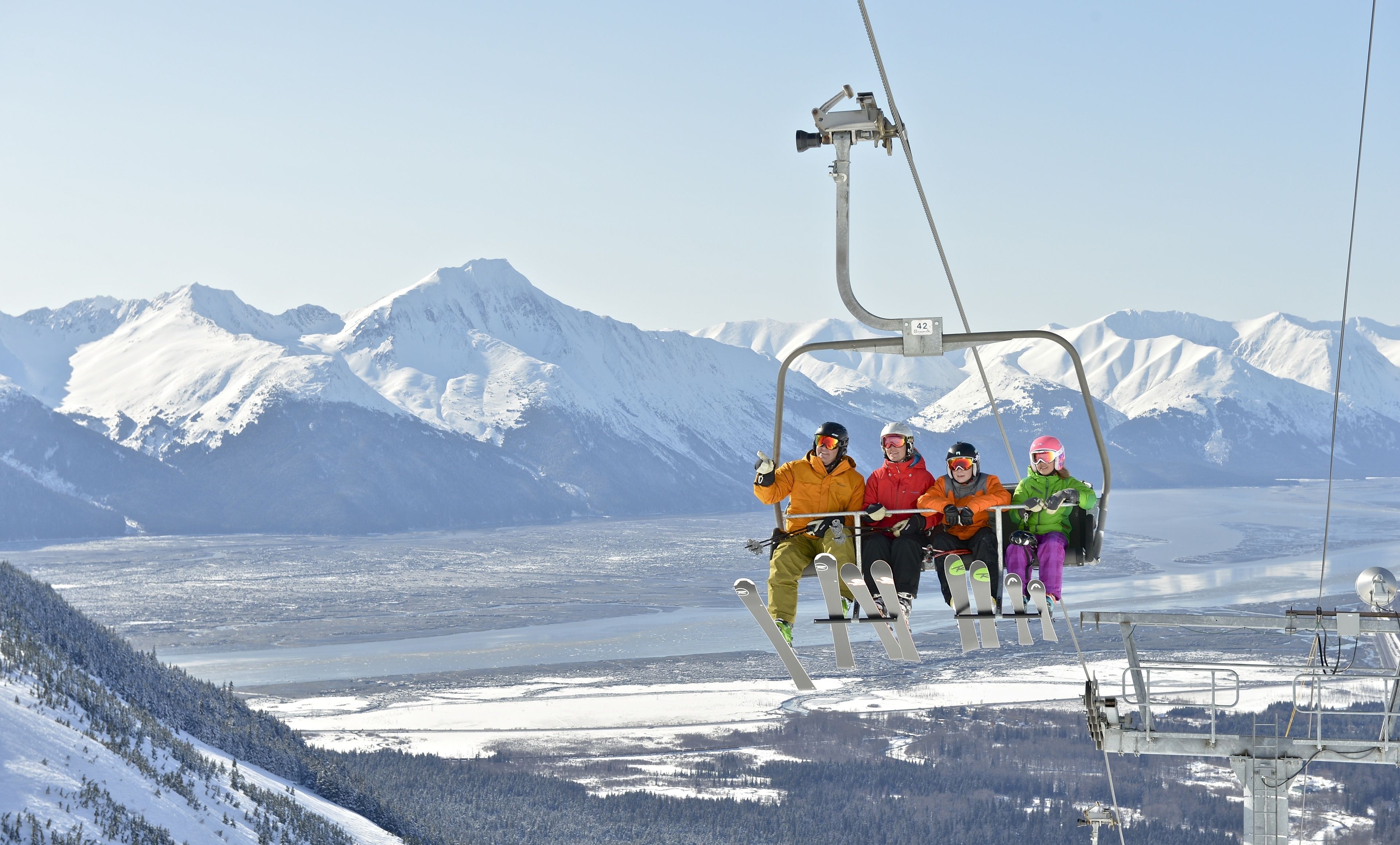 A group of people on a ski lift with snow-covered mountains in the background.