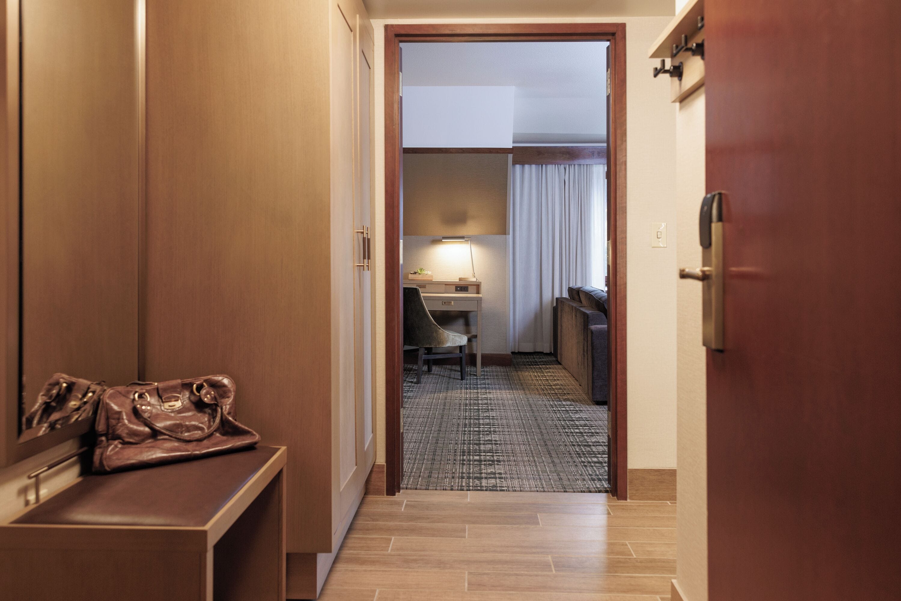 A hotel hallway with a desk, chair, and a handbag on a counter.