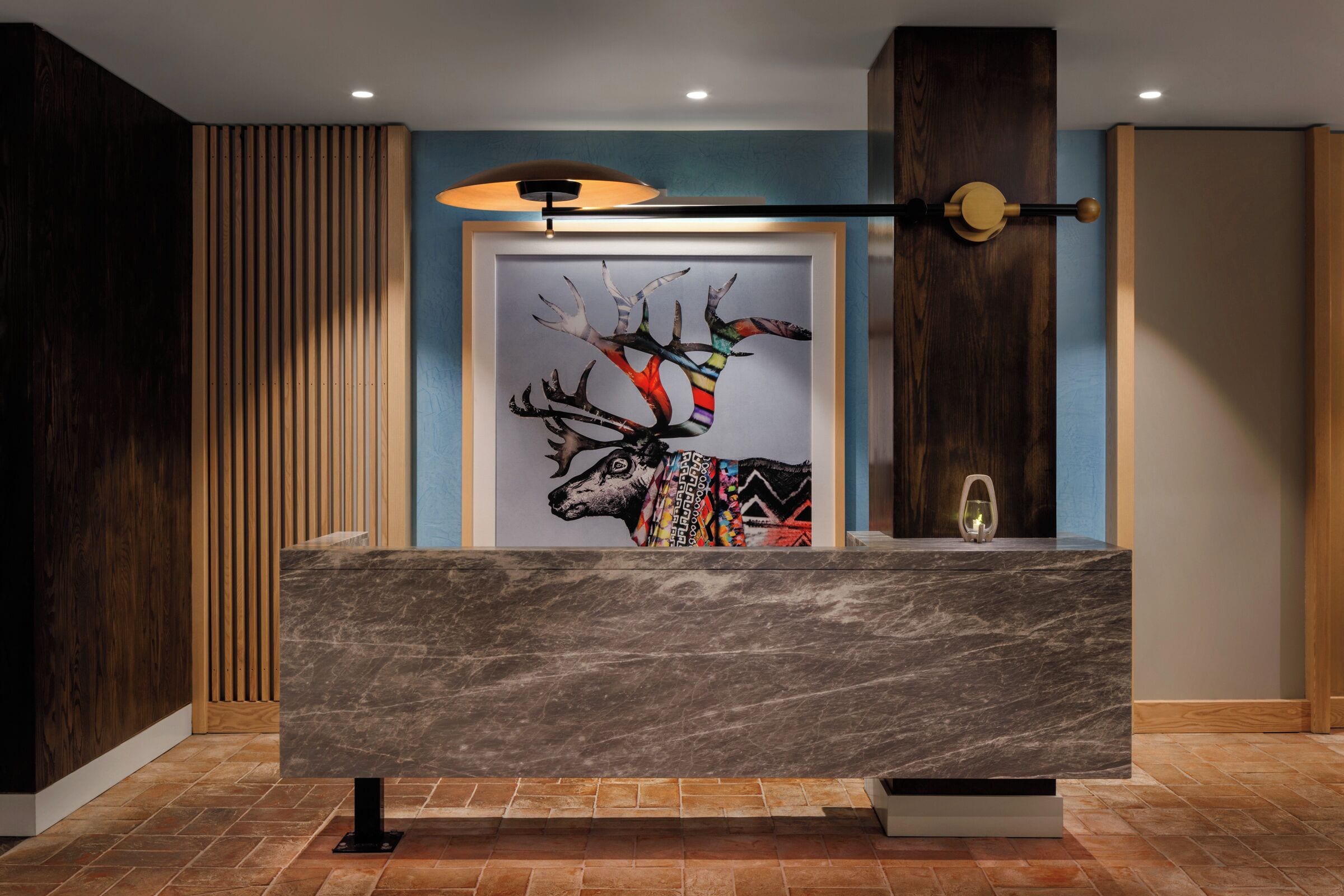 A reception desk with a marble top, a framed artwork of a deer, and a wall-mounted light fixture.