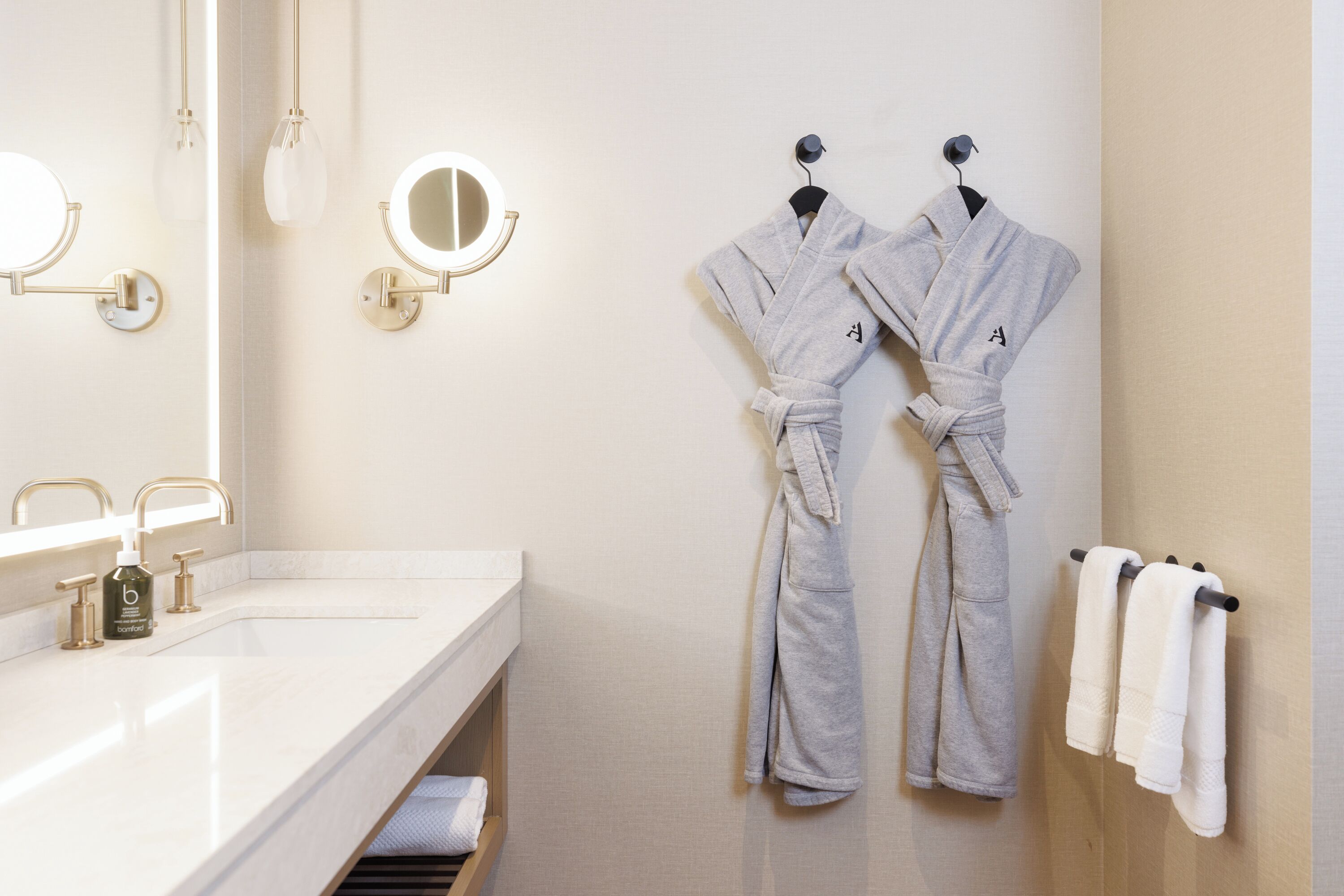A bathroom with a white sink, two mirrors, and two robes hanging on hooks.