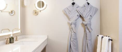 A bathroom with a white sink, two mirrors, and two robes hanging on hooks.