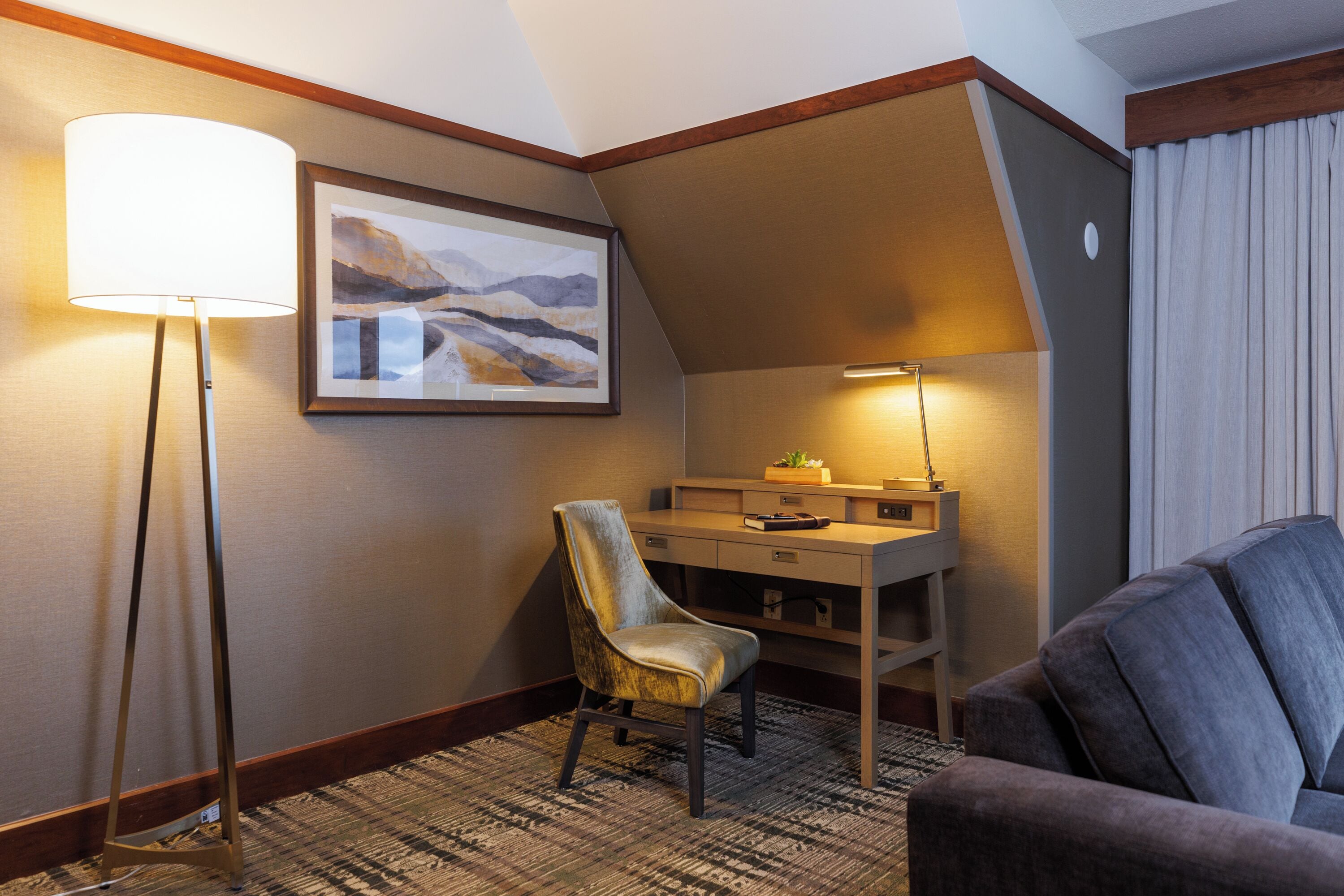 Una habitación de hotel con un escritorio, una silla, una lámpara y un sofá.