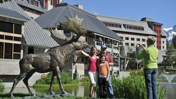 A family posing with a moose statue in front of a building with a sloped roof and a pond nearby.