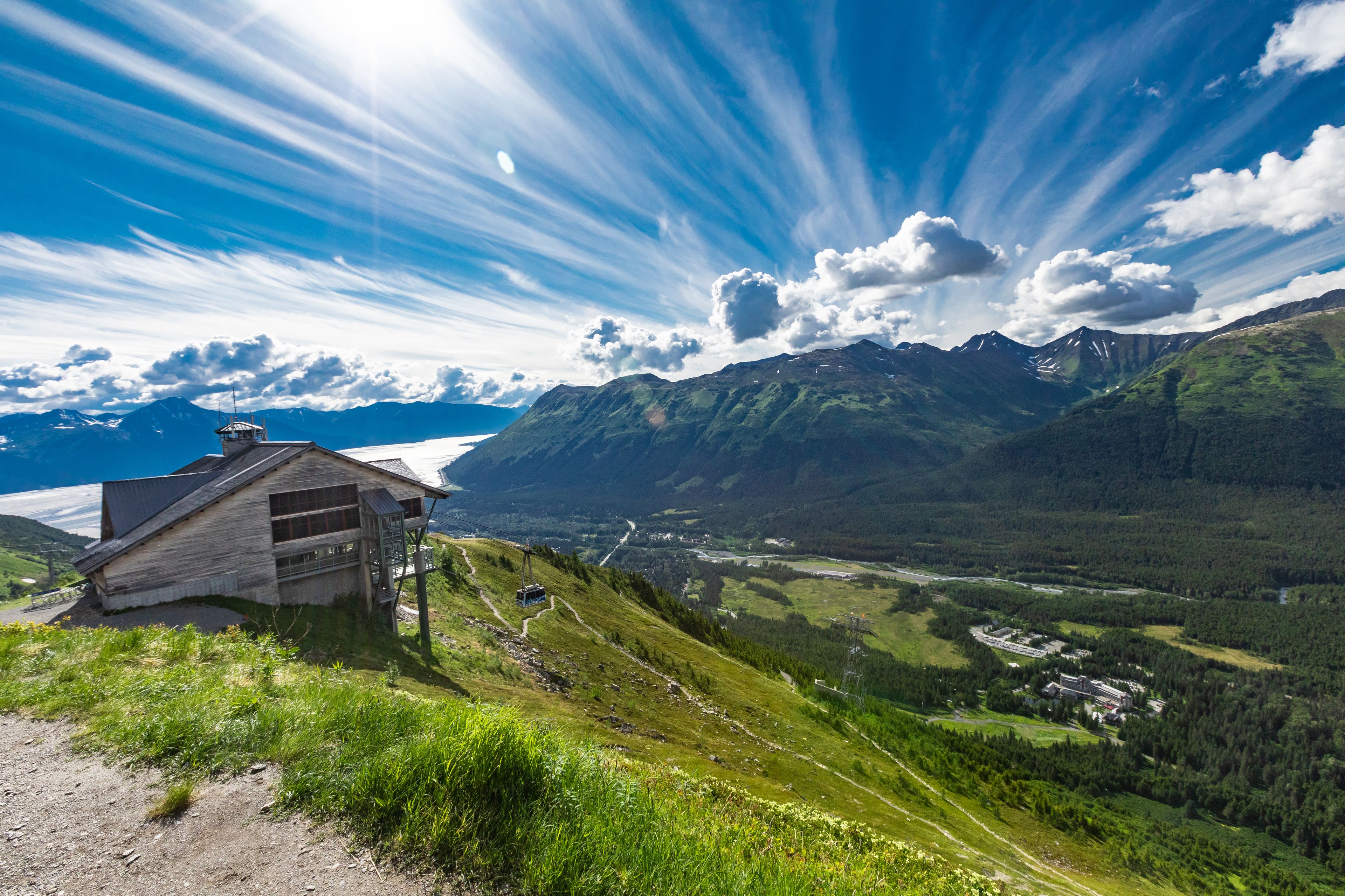 Een houten hutje met een metalen dak, gelegen in een bergachtig landschap onder een heldere lucht.
