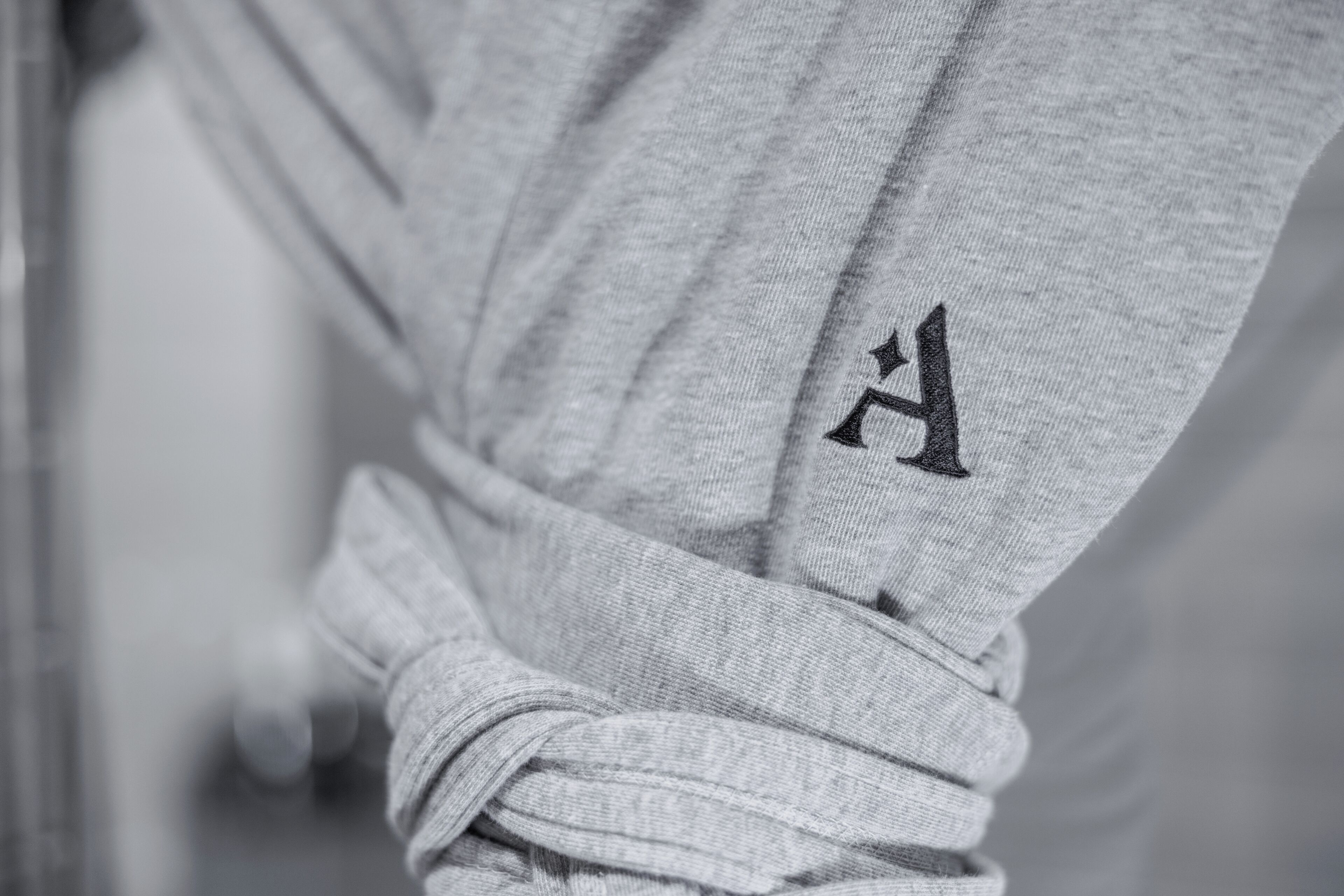 A close-up of a grey fabric with a black embroidered letter 'H'.