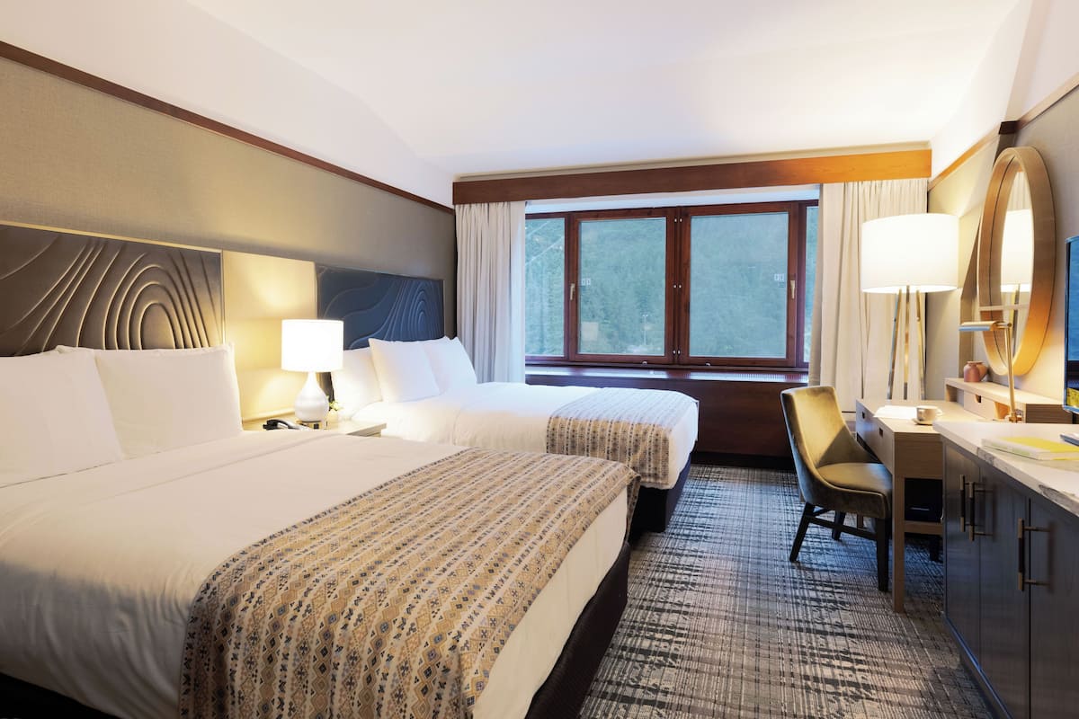 A hotel room with two beds, a desk, a chair, and a large window.