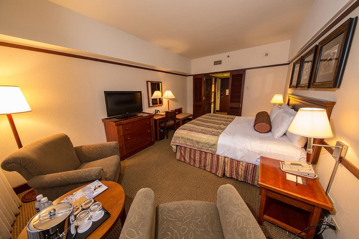 A hotel room with a bed, two armchairs, a desk, a television, and a dining table with a tray of breakfast items.